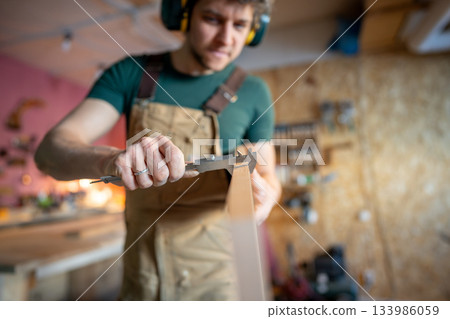 Work with vernier calipers to check wood plank thickness. Close up skilled craftsman woodworking Work with vernier calipers to check wood plank thickness. Close up skilled craftsman woodworking 133986059