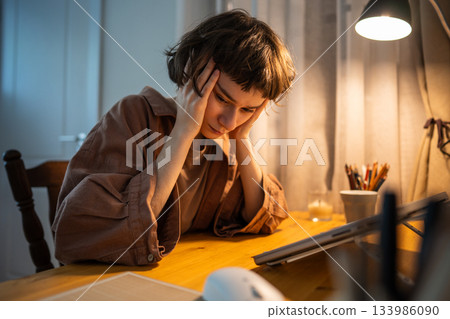 Tired woman with head in hands battling stress after late home shift wuth laptop. Headache stress 133986090