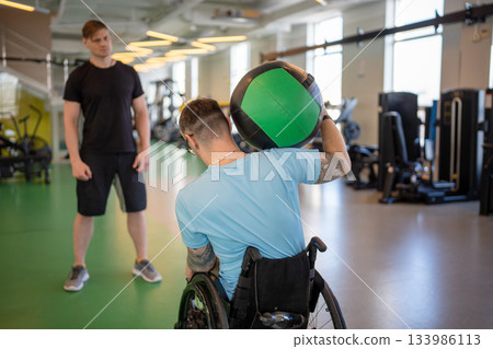 Rearview wheelchair man lean to sides to limit with medicine ball, raise for neck muscles work Rearview wheelchair man lean to sides to limit with medicine ball, raise for neck muscles work 133986113
