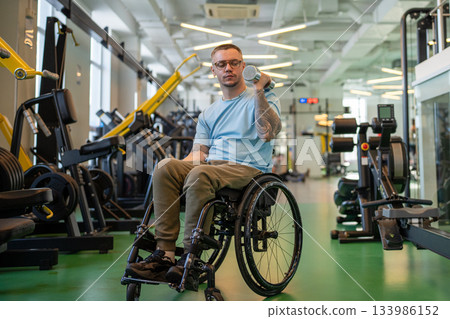 Man athlete in wheelchair working out with dumbbells to build strong arm muscles at sports center. Man athlete in wheelchair working out with dumbbells to build strong arm muscles at sports center. 133986152