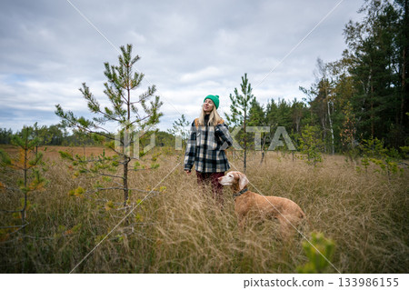 Female hiker pet owner on morning walk outdoors with dog in autumn wetland on overcast fall day. Female hiker pet owner on morning walk outdoors with dog in autumn wetland on overcast fall day. 133986155