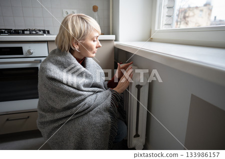 Woman warming hands on battery at home during winter. inadequate heating highlight, coldness indoor. Woman warming hands on battery at home during winter. inadequate heating highlight, coldness indoor. 133986157