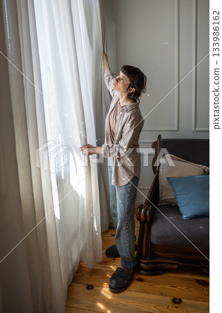 Calm woman removing curtains for laundry and home decor update on weekend day, household chores 133986162