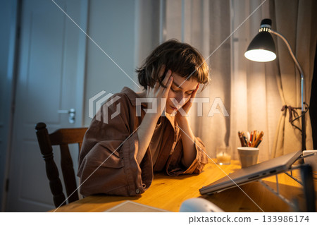 Tired young woman rub temples with head buried in hands overwhelmed by headache and fatigue Tired young woman rub temples with head buried in hands overwhelmed by headache and fatigue 133986174
