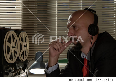 Bald man in headphones listening to music, listening and recording conversations, watching and controlling people, the average plan 133986183