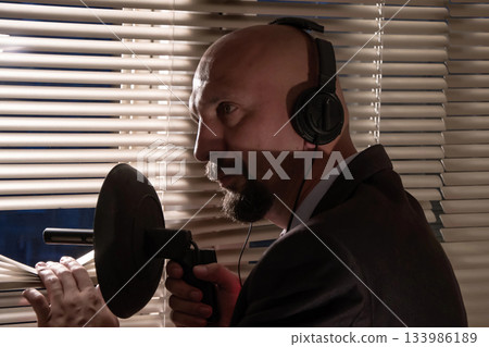 Secret agent secretly eavesdropping directional microphone pushing the blinds, surveillance and control of people, the average plan 133986189