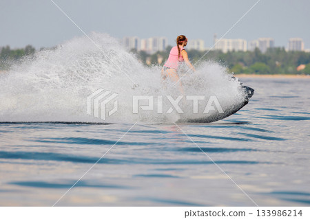 athletic girl rides a jet ski with splashes, she is having fun on a jet ski with splashes in the waters of the Gulf of Finland, Russia, St.Petersburg athletic girl rides a jet ski with splashes, she is having fun on a jet ski with splashes in the waters of the Gulf of Finland, Russia, St.Petersburg 133986214