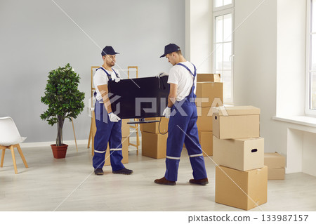 Young mover male team carrying tv set for moving, individual or company worker job moving things 133987157