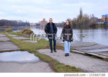 father and daughter are walking in the cold season near the lake in autumn, early winter, puddles 133987190