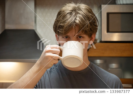 Drinking coffee young caucasian man in home kitchen interior during morning routine, relaxed lifestyle, indoor cozy breakfast moment, everyday life concept. 133987377