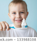 Young boy holding a toothbrush with a large amount of white toothpaste in the shape of a Christmas tree swirled on it. AI image 133988108