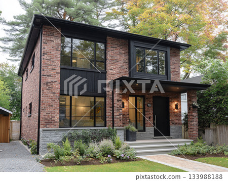 A modern luxury house featuring dark red brick, black-framed windows, a slate roof, and a large integrated garage, surrounded by lush mature trees and a paved driveway. A modern luxury house featuring dark red brick, black-framed windows, a slate roof, and a large integrated garage, surrounded by lush mature trees and a paved driveway. 133988188