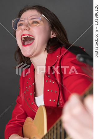 Happy young woman guitarist in state of pure joy playing classical guitar with passion, her mouth wide open, voice resonating with powerful emotion as she belts out song that hits right in heart Happy young woman guitarist in state of pure joy playing classical guitar with passion, her mouth wide open, voice resonating with powerful emotion as she belts out song that hits right in heart 133990126
