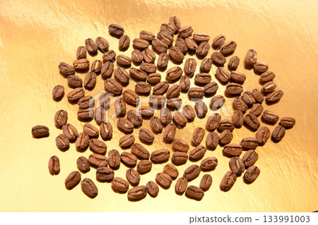 A collection of roasted coffee beans shaped into an oval on a shiny gold background 133991003