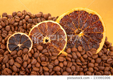 Roasted coffee beans surround dried orange slices on a golden reflective surface Roasted coffee beans surround dried orange slices on a golden reflective surface 133991006