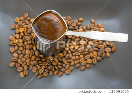 Stylish close-up of a cezve with aromatic Turkish coffee on a gray surface with coffee beans 133991025