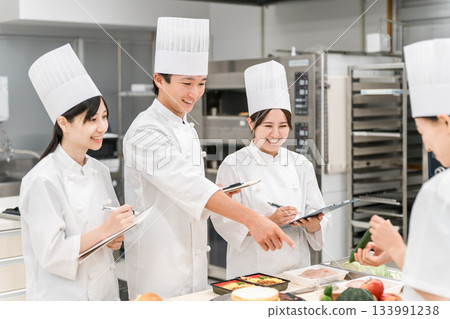 Male and female chefs dressed in cook uniforms developing menus, products, and recipes in the kitchen 133991238