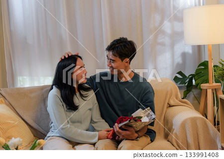 Happy young couple share tender love at cozy home, man gives woman beautiful romantic valentine day flowers, celebrating special intimate moment indoors with warm light. Happy young couple share tender love at cozy home, man gives woman beautiful romantic valentine day flowers, celebrating special intimate moment indoors with warm light. 133991408