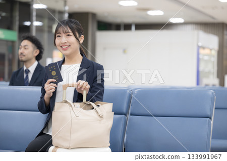 一位商務女性坐在候機大樓裡，手裡拿著護照。這是在機場或車站候機大樓進行的商務旅行場景，畫面中可以看到她的上半身。 133991967