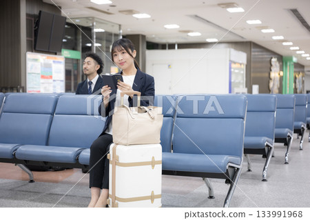 一位商務女性坐在候機大樓裡,手裡拿著護照。這是在機場或車站候機大樓的商務旅行場景。全身照。 一位商務女性坐在候機大樓裡,手裡拿著護照。這是在機場或車站候機大樓的商務旅行場景。全身照。 133991968