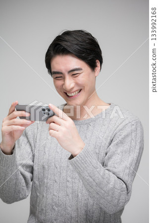 Handsome smiling man watching a video on his smartphone Gray background Vertical Handsome smiling man watching a video on his smartphone Gray background Vertical 133992168