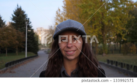 A woman with long, curly hair wearing a gray cap enjoys a relaxed moment while walking on a serene path surrounded by vibrant autumn leaves and peaceful trees. A woman with long, curly hair wearing a gray cap enjoys a relaxed moment while walking on a serene path surrounded by vibrant autumn leaves and peaceful trees. 133992571