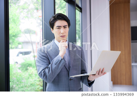 A man in a suit holding a laptop. Image of a consultant, recruiter, or other job change. Worried, thinking, troubled expression. 133994369