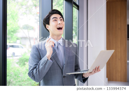 一位身穿西裝的男士手持筆記型電腦,面帶微笑,似乎正在思考某個想法。形象可能是顧問、招募人員等。 一位身穿西裝的男士手持筆記型電腦,面帶微笑,似乎正在思考某個想法。形象可能是顧問、招募人員等。 133994374