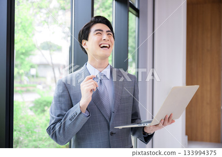 一個身穿西裝、手持筆記型電腦、微笑、似乎想到了什麼的男人。可能是顧問、招募人員等等。 133994375