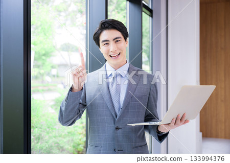 A man in a suit holding a laptop. Image of a consultant, recruiter, or other job change. Smiling and looking at the camera. A man in a suit holding a laptop. Image of a consultant, recruiter, or other job change. Smiling and looking at the camera. 133994376