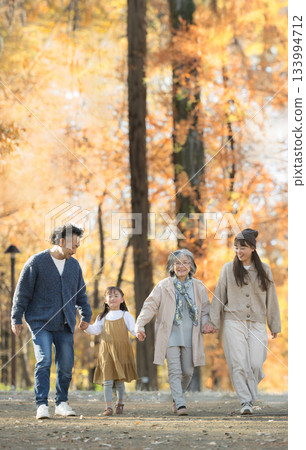 Autumn family photo: Smiling three-generation family in a forest of autumn leaves. Grandmother, grandchild and child couple walking hand in hand. Portrait Autumn family photo: Smiling three-generation family in a forest of autumn leaves. Grandmother, grandchild and child couple walking hand in hand. Portrait 133994712