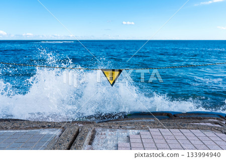 Caution signs and wave spray on the beach 133994940