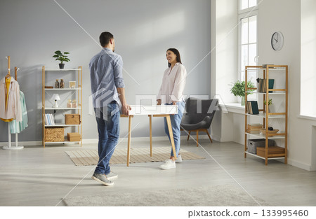 Happy young husband and wife moving furniture and carrying a new table together 133995460