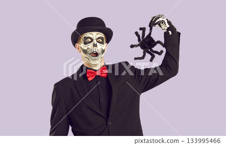 Funny surprised man dressed in skeleton Halloween costume holding spooky toy spider Funny surprised man dressed in skeleton Halloween costume holding spooky toy spider 133995466