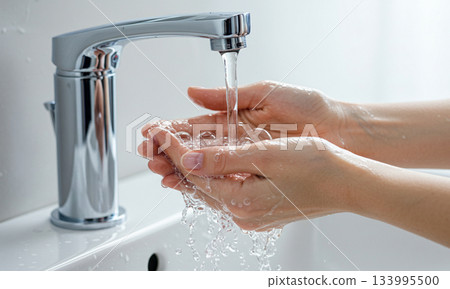 Close-up of hands covered in soap lather and running water over a white bathroom sink Close-up of hands covered in soap lather and running water over a white bathroom sink 133995500