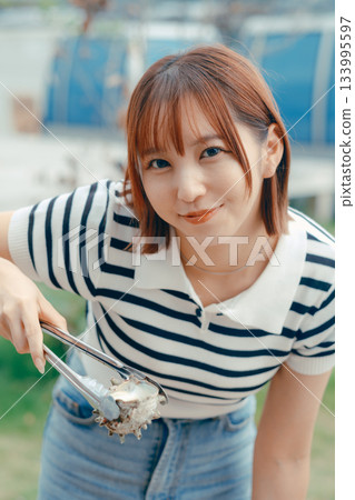 一位二十多歲的女子在海灘上烤海鮮 一位二十多歲的女子在海灘上烤海鮮 133995597