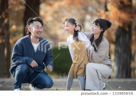 Family playing in the autumn park. A commemorative photo of smiling parents and children in a forest of autumn leaves. A heartwarming image of outings and leisure time memories. Family playing in the autumn park. A commemorative photo of smiling parents and children in a forest of autumn leaves. A heartwarming image of outings and leisure time memories. 133995659