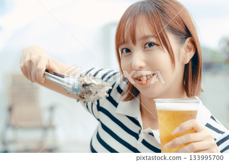 A woman in her 20s enjoying beer while grilling seafood 133995700