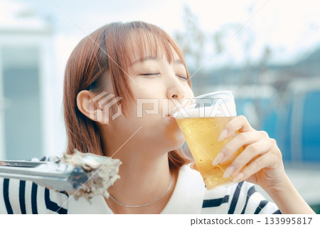 一位二十多歲的女子一邊享用啤酒,一邊燒烤海鮮。 一位二十多歲的女子一邊享用啤酒,一邊燒烤海鮮。 133995817