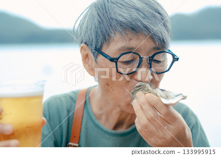 A scene of a senior woman enjoying beer and oysters at the beach 133995915
