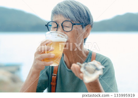 一位老婦人在海灘上享用啤酒和牡蠣的場景 133995919