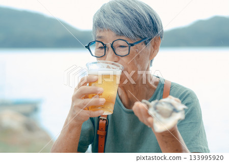 一位老婦人在海灘上享用啤酒和牡蠣的場景 一位老婦人在海灘上享用啤酒和牡蠣的場景 133995920