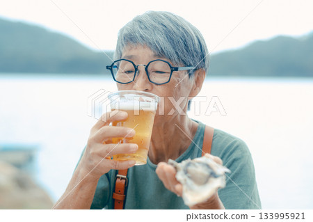 一位老婦人在海灘上享用啤酒和牡蠣的場景 一位老婦人在海灘上享用啤酒和牡蠣的場景 133995921