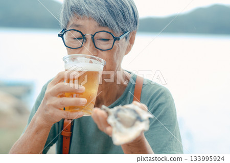 一位老婦人在海灘上享用啤酒和牡蠣的場景 133995924