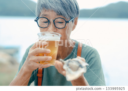 一位老婦人在海灘上享用啤酒和牡蠣的場景 133995925