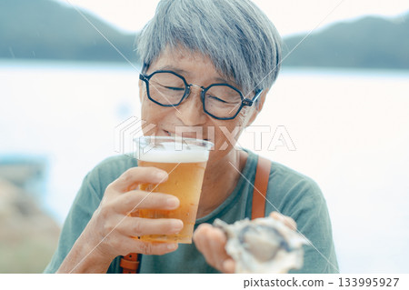 一位老婦人在海灘上享用啤酒和牡蠣的場景 133995927