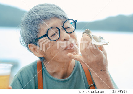 一位老婦人在海灘上享用啤酒和牡蠣的場景 133995931