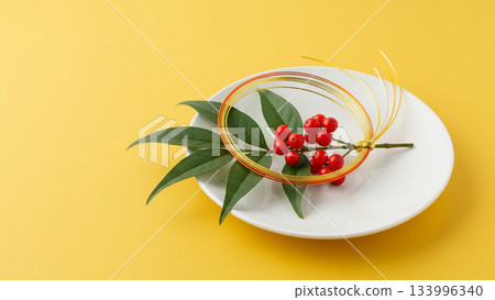 一幅日式新年圖片，畫面中黃底上掛著南天竹和梅花形狀的水引線。 133996340