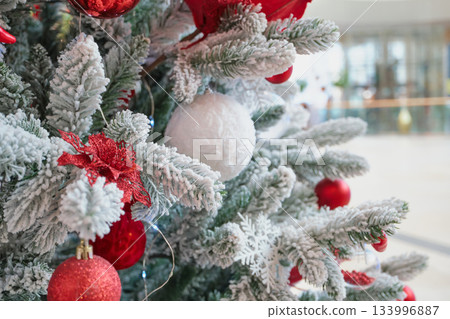 Flocked artificial pine branches decorated with red balls, white ornaments and poinsettia in Shopping Mall Flocked artificial pine branches decorated with red balls, white ornaments and poinsettia in Shopping Mall 133996887