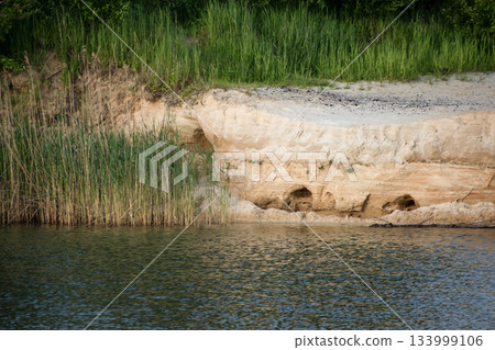 Tranquil riverside scene showcasing a sandy bank with vibrant green grass, creating a serene atmosphere Tranquil riverside scene showcasing a sandy bank with vibrant green grass, creating a serene atmosphere 133999106